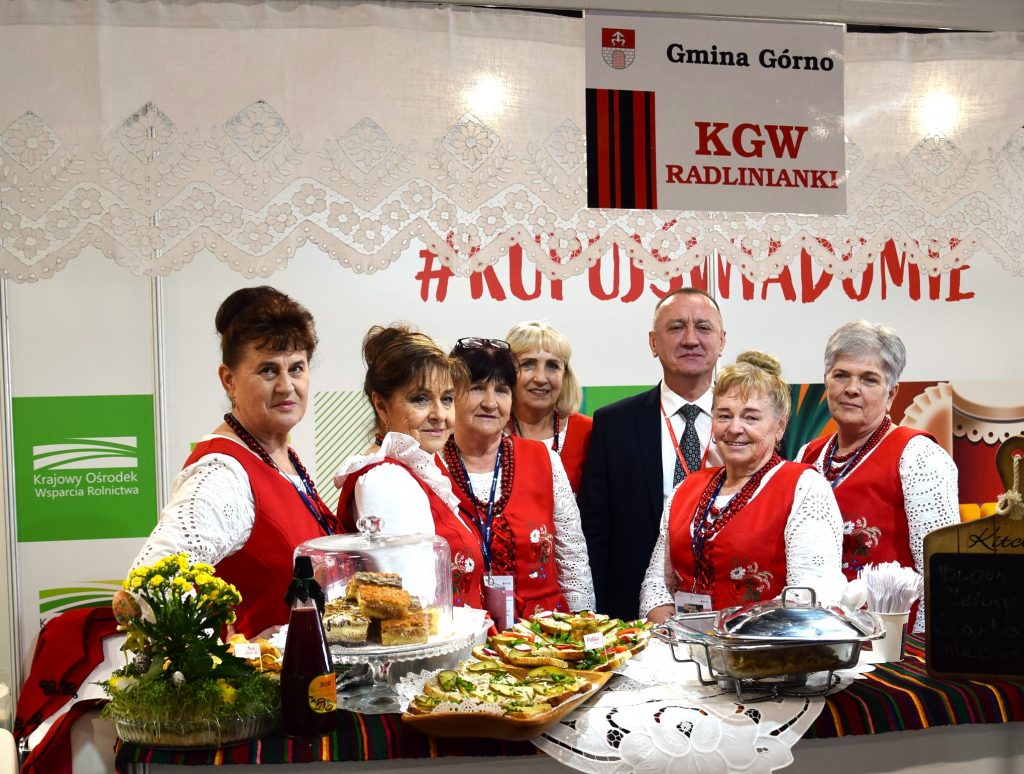 Mężczyzna w garniturze, Robert Jurek, stoi przy stoisku z regionalnymi przekąskami podczas Targi Agro&Active Travel 2026, otoczony przez przedstawicielki Koła Gospodyń Wiejskich.