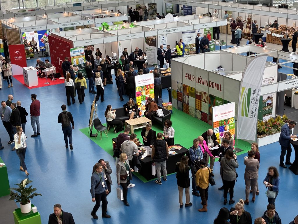 Hala wystawiennicza podczas Europejskiego Forum Rolniczego – liczne stoiska branżowe, w tym „Kupuj Świadomie”, oraz uczestnicy rozmawiający i zwiedzający ekspozycje w nowoczesnym, przeszklonym obiekcie.