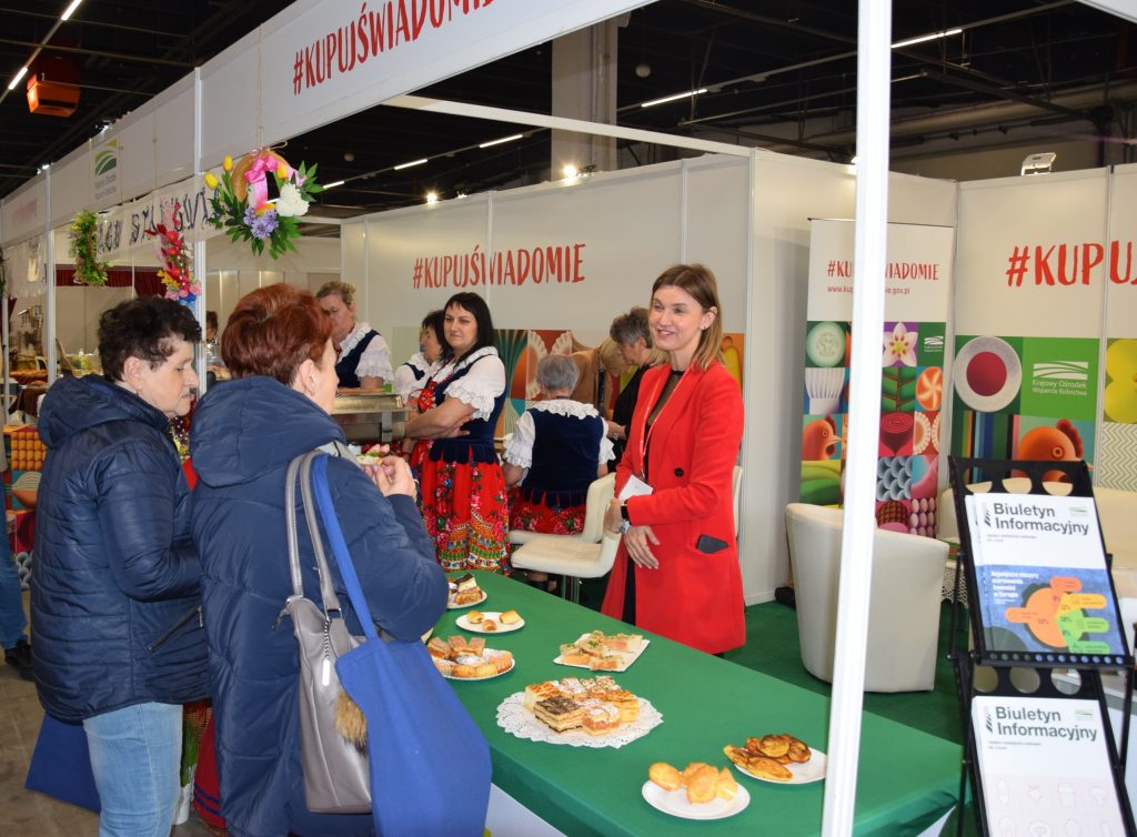 Na stoisku promującym ideę #KupujŚwiadomie podczas Targi Agro&Active Travel 2026 grupa kobiet w strojach ludowych prezentuje regionalne potrawy. Wśród nich znajduje się Anna Wołowiec